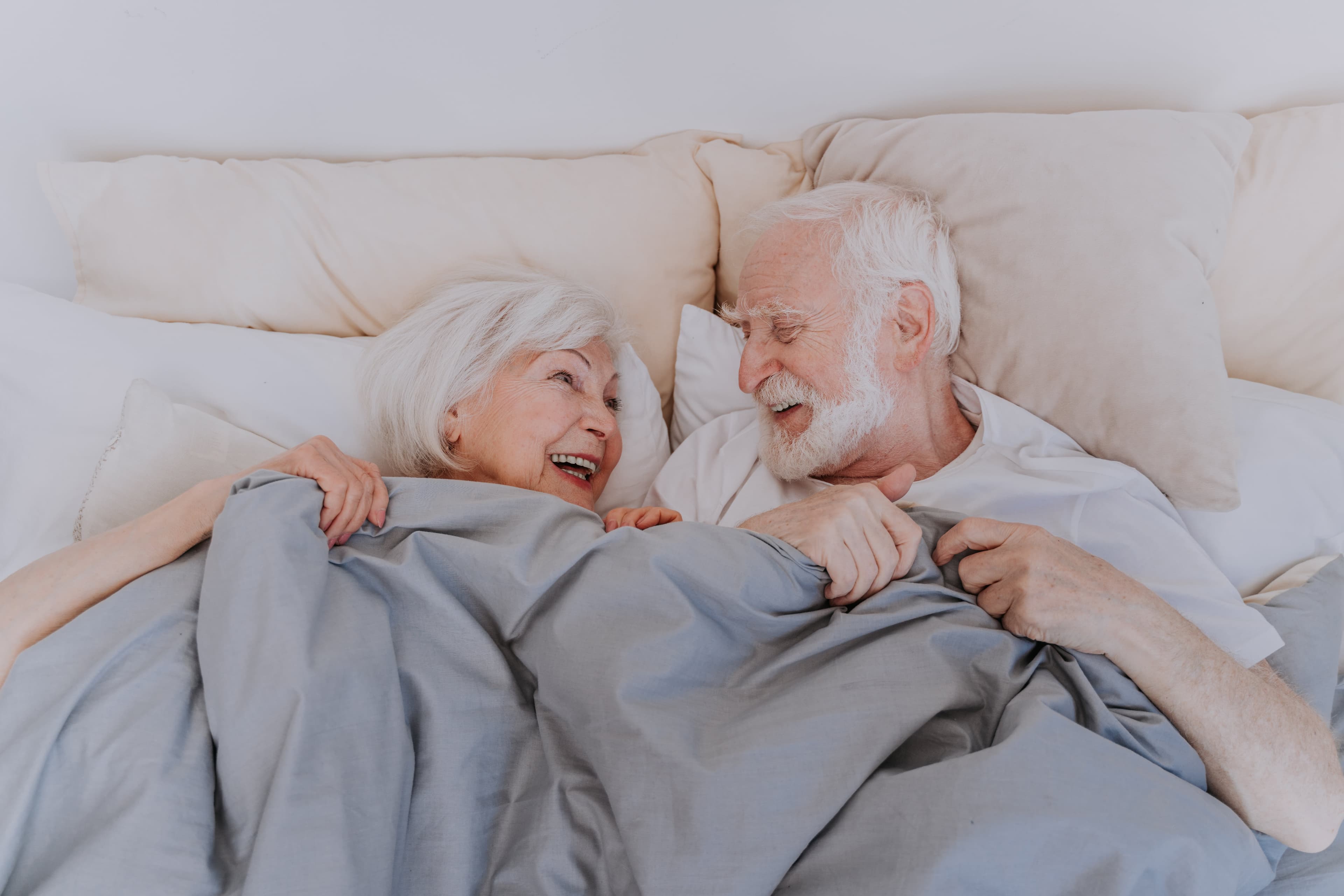 An elderly couple in bed laughing happily together